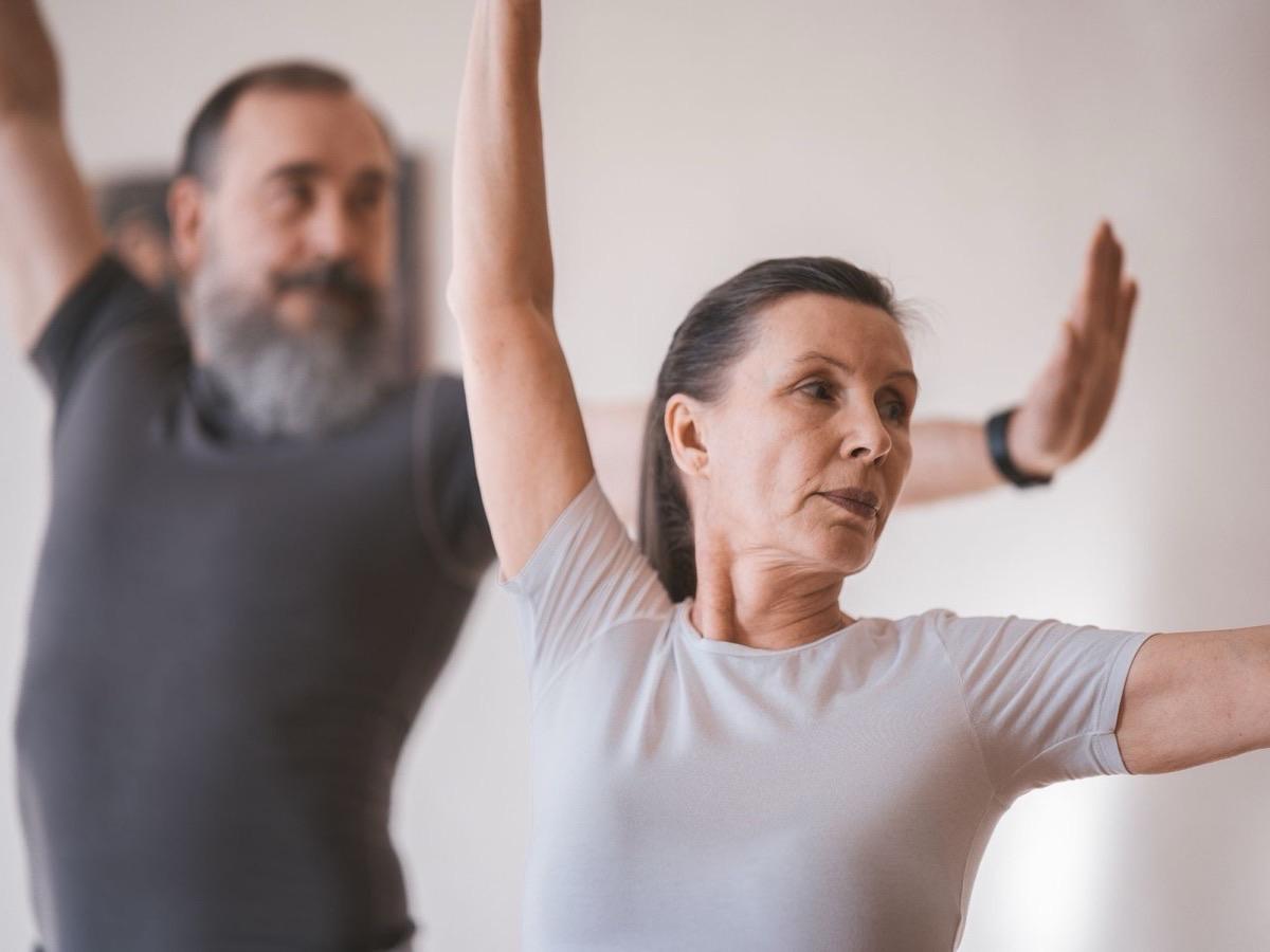 An older woman and man holding a steady standing balance pose with arms extended